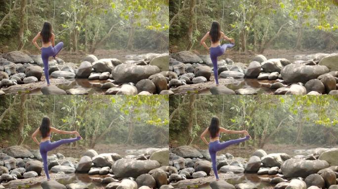 4k慢，亚洲年轻迷人的女人正在白色套房的瀑布练习瑜伽。放松并集中精力于大自然。女人的手在冥想，莲花姿