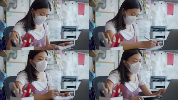 亚洲女商人戴着口罩，在家庭办公室工作，使用平板电脑，智能手机和笔记本电脑。戴上口罩，以防止与他人连接