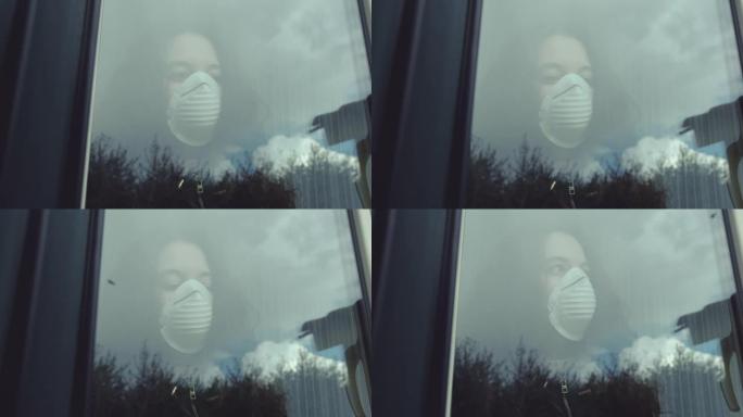 沉思的年轻女子戴着口罩，在看着窗外时保护自己免受新型冠状病毒肺炎。一只飞行中的鸟被反射在窗户玻璃上