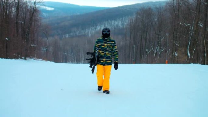 戴着安全眼镜的专业滑雪者沿着白雪皑皑的跑道上升。滑雪者拿着滑雪板。美丽的冬季风景。