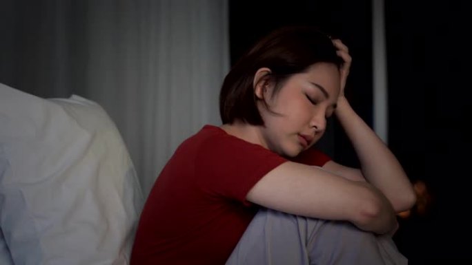 4k郁闷年轻美丽的亚洲女人独自坐在床上拥抱膝盖哭泣。不快乐的压力女人十几岁的女孩在卧室里休息，情绪消