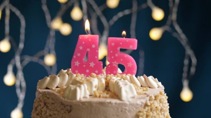 蓝色背景上有45号粉色蜡烛的生日蛋糕。蜡烛吹灭了。慢动作和特写视图