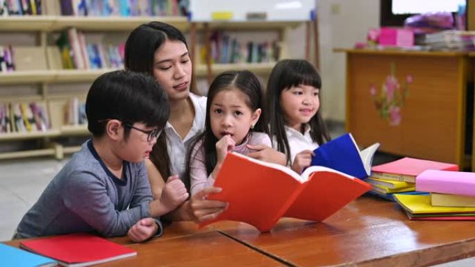 一群亚洲孩子与老师一起在学校图书馆读书，背景书架
