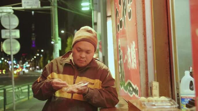 亚洲男子晚上在街头夜市吃热章鱼烧。