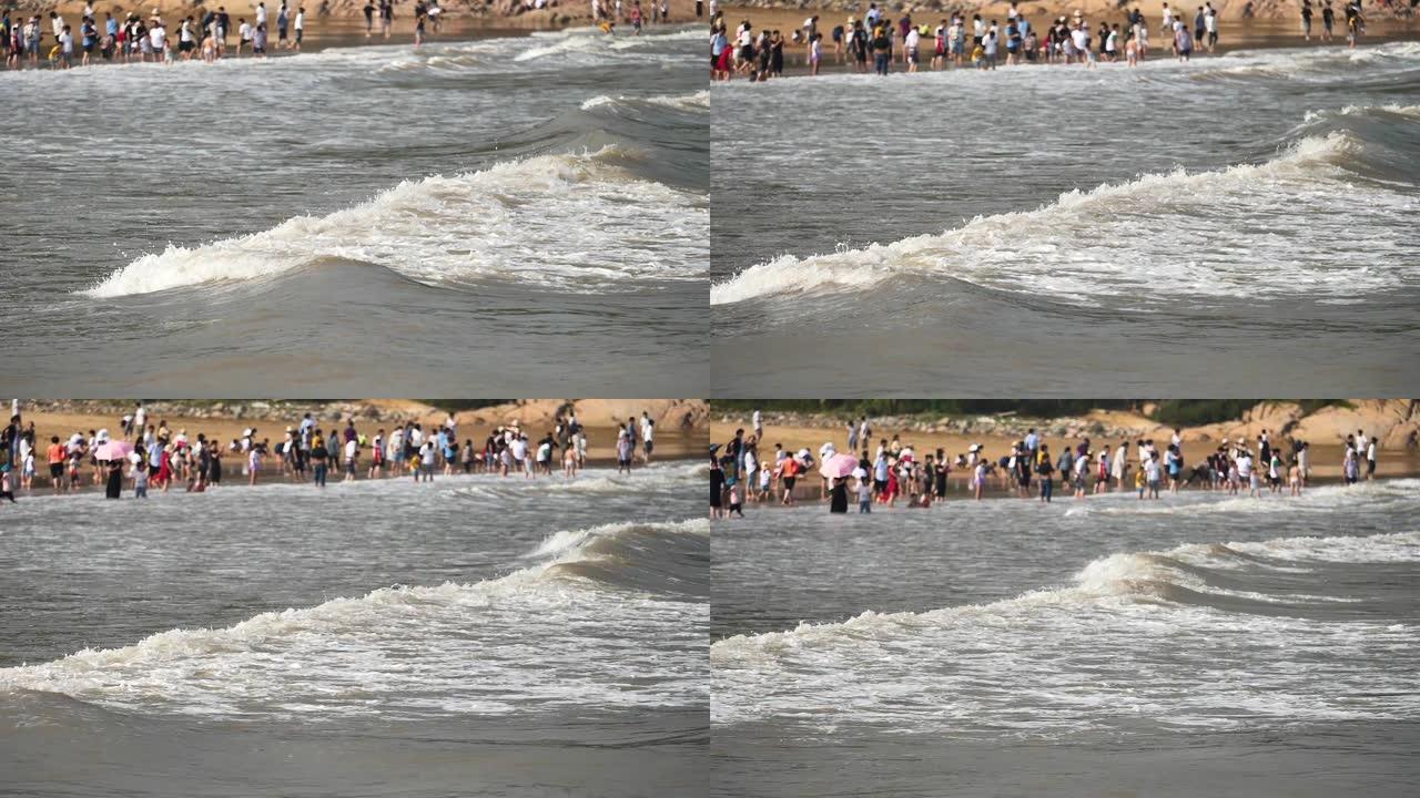 拥挤的游客背景，相机平移，高速，超慢动作，180 FPS的泥泞海滩上的波浪特写。