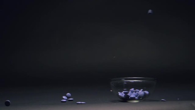 蓝色糖果在慢动作中掉落在玻璃碗中，黑色黑板纹理背景上的复制空间