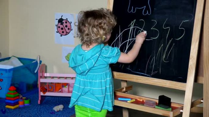 有趣的小孩可爱的金发学步女孩在黑板上用粉笔画画