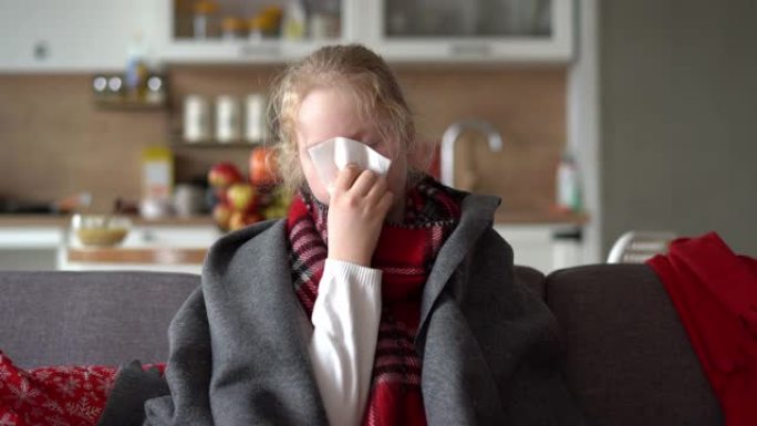 家里冷酷的高加索女孩。一个生病的孩子的肖像穿着围巾和格子在公寓的沙发上，女学生将sno吹入餐巾纸