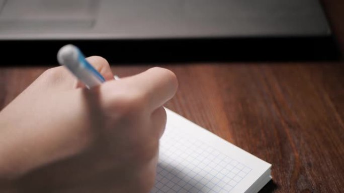 女手用笔在笔记本上写东西，旁边是笔记本电脑。特写慢动作