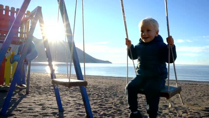 三岁男孩在阳光明媚的早晨在沙滩上荡秋千