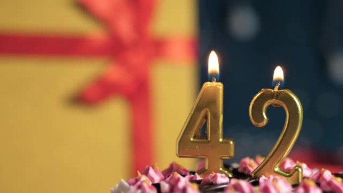 生日蛋糕编号42点灯燃烧的金色蜡烛，蓝色背景礼物黄色盒子用红丝带绑起来。特写和慢动作