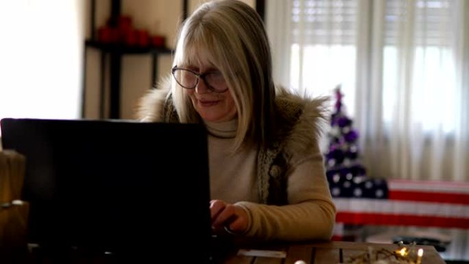 年长的女人在家在笔记本电脑键盘上打字