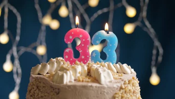 蓝色背景上有33号粉色蜡烛的生日蛋糕。蜡烛吹灭了。慢动作和特写视图