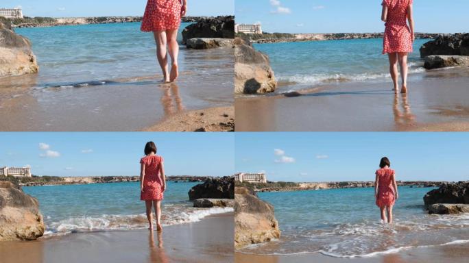 年轻的高加索女孩在海边下水。穿着红色短裙的黑发女孩走在海边。迷人的女人走过海边。穿着红色连衣裙的年轻