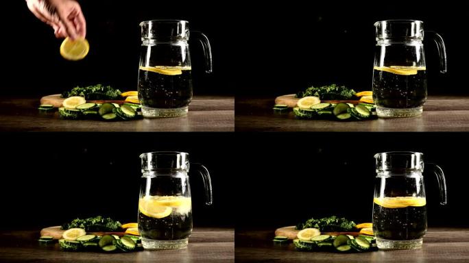 将柠檬黄瓜和薄荷叶切成薄片，放在装有苏打水的玻璃水瓶旁边的木制切菜板上。男性手在一杯苏打水中扔柠檬片