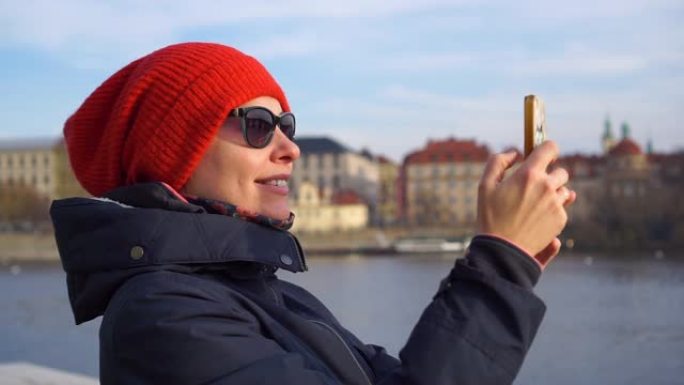 布拉格捷克戴着红帽子的年轻漂亮女人游客用智能手机微笑拍照