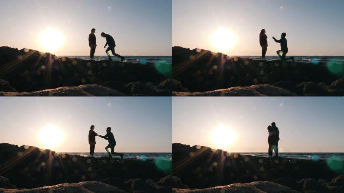 害羞的有魅力的男人站在膝盖上，在日落时向女友求婚。幸福的年轻夫妇在日落时在海边接吻和拥抱。求婚男人的
