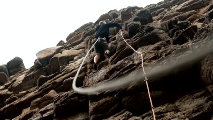 一名男性登山者为在雨中攀登岩石路线的绳索提供保险。