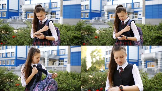 一名学生站在学校门前，妈妈发短信，把手机放在背包里。放学后的少女回家了。