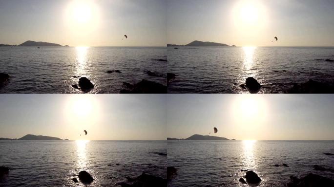 美丽的阳光日落在金色黄昏日落时平静的海洋水面在地平线上美丽的风景夏天黄昏黄昏和旅行的人玩滑翔伞在海上