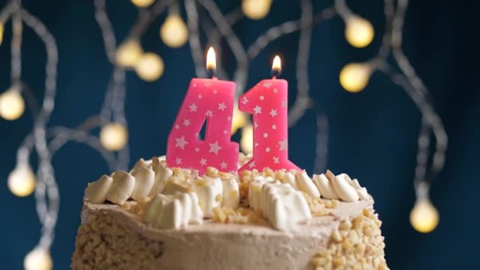 蓝色背景上有41号粉色蜡烛的生日蛋糕。蜡烛吹灭了。慢动作和特写视图