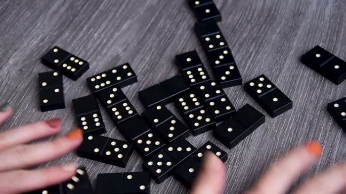 在木桌上玩多米诺骨牌。多米诺骨牌女人的手。休闲游戏概念。选择性聚焦。