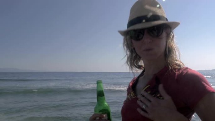 一个漂亮的年轻女子带着啤酒在沙滩上散步