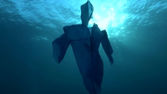 蓝色塑料雨衣作为幽灵在蓝色的水中慢慢漂浮。海洋的水下塑料污染。塑料垃圾环境污染问题。慢动作