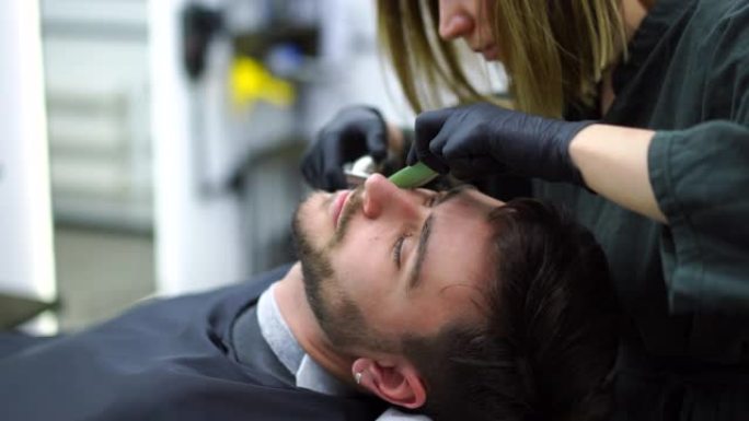 年轻美丽的高加索女人理发师在现代理发店剪胡子英俊的男人