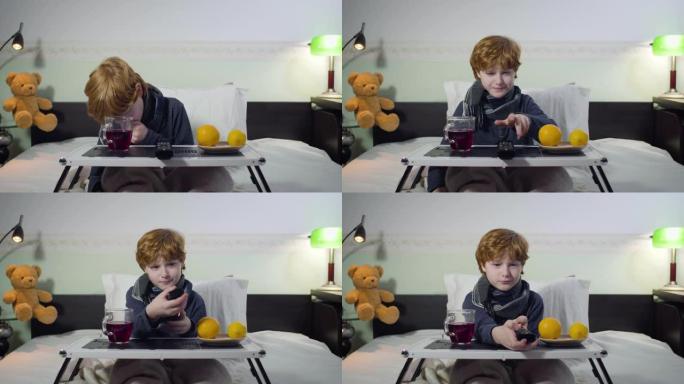 咳嗽的白人小男孩拿遥控器和切换电视频道的肖像。红发可爱的孩子坐在托盘前的床上，端着茶和橘子。疾病，健