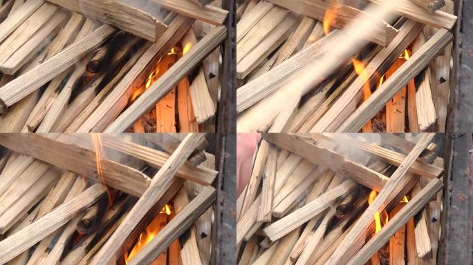 一个人用堆放的柴火生火。准备烧烤。特写。在便携式烧烤炉中，新鲜点燃的烧烤炉与燃烧的木头原木一起点燃小