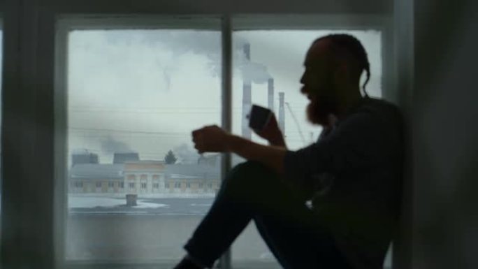 一个留着胡须的红发男人的肖像坐在窗户旁边，背景是烟斗冒烟。