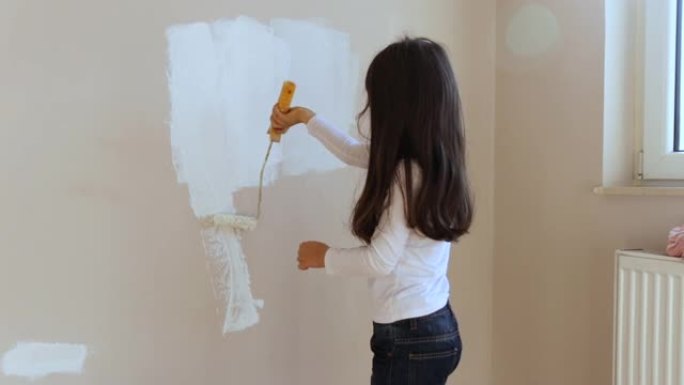 可爱的小女孩使用油漆滚筒和白色油漆墙