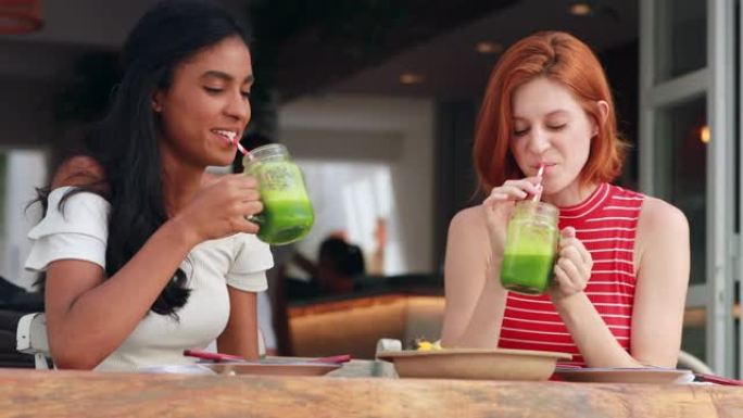 两个种族差异很大的女孩在外面喝健康的绿色排毒汁