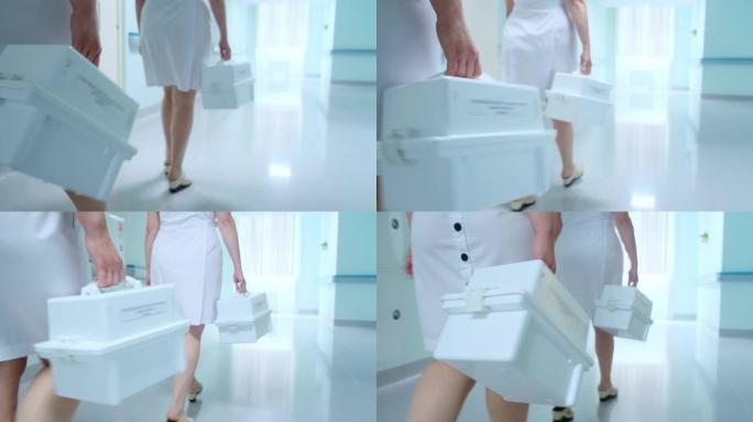 穿着白大褂的妇女沿着医院走廊走，并携带白色盒子