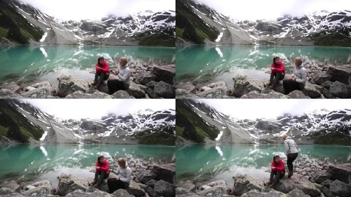 两个女人坐在高山湖泊附近的岩石上。