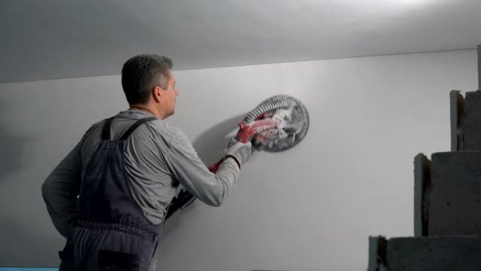 木匠在新公寓墙上使用电动砂光机节省时间