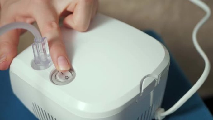 女性手指按下喷雾器上的电源按钮进行吸入。按钮开始闪烁蓝色。慢动作和特写