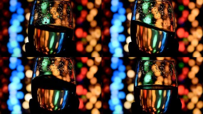 在散焦的深色背景上，在玻璃杯中挥舞金色白葡萄酒。美丽的葡萄酒广告素材。侍酒师在酒杯中混合葡萄酒，评估
