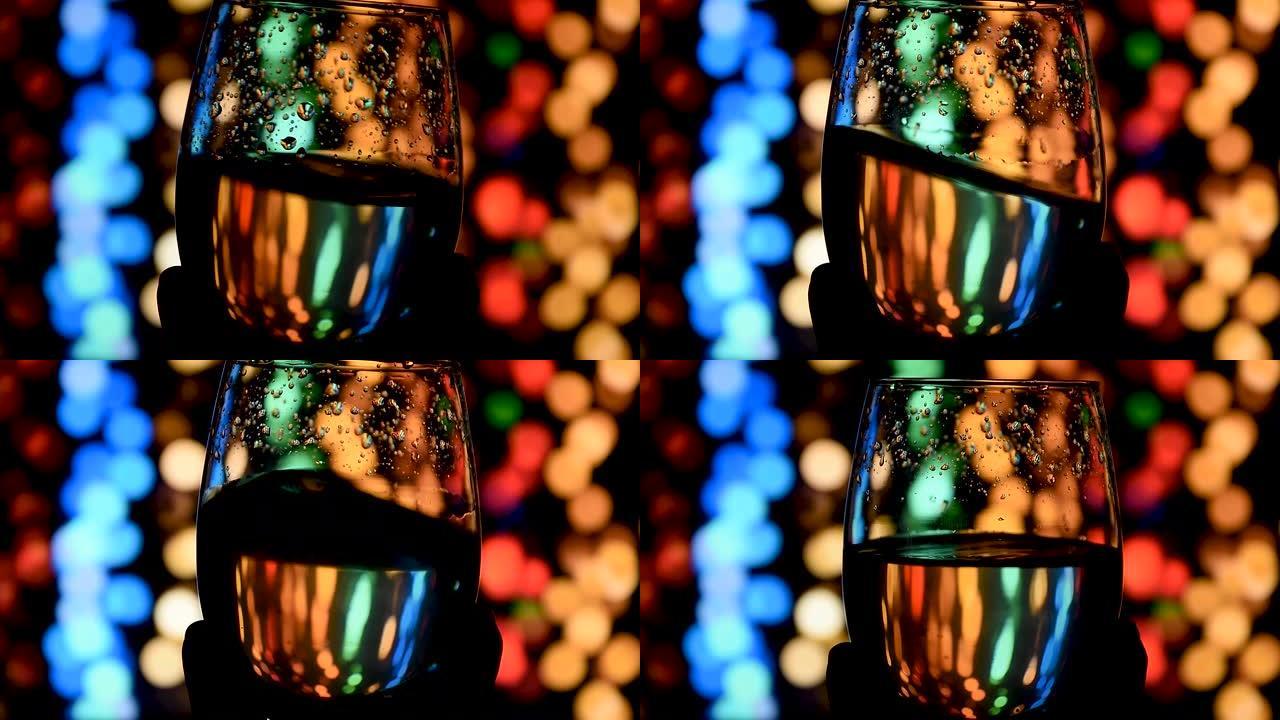 在散焦的深色背景上，在玻璃杯中挥舞金色白葡萄酒。美丽的葡萄酒广告素材。侍酒师在酒杯中混合葡萄酒，评估