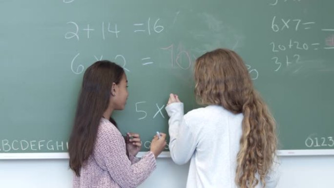 一个镜头对准了两个正在黑板上写字的小学生的后背
