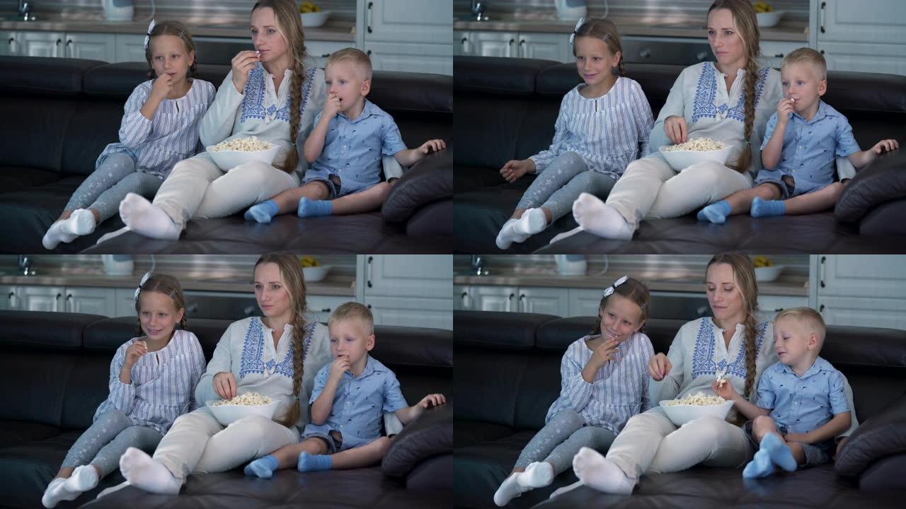 妈妈和两个孩子坐在沙发上吃爆米花和看电视