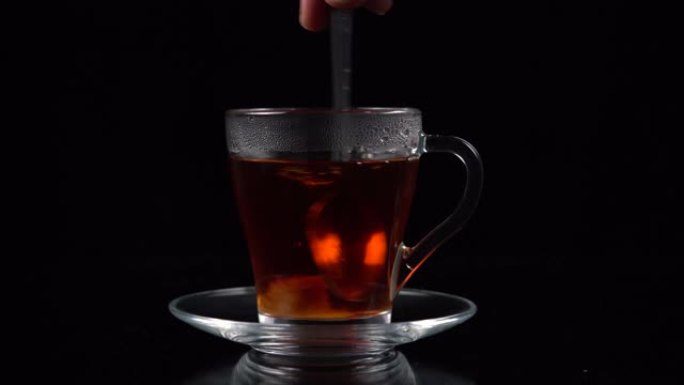 将一立方蔗糖浸入一杯茶中，并用勺子在黑色背景上搅拌。