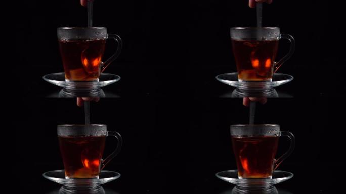 将一立方蔗糖浸入一杯茶中，并用勺子在黑色背景上搅拌。