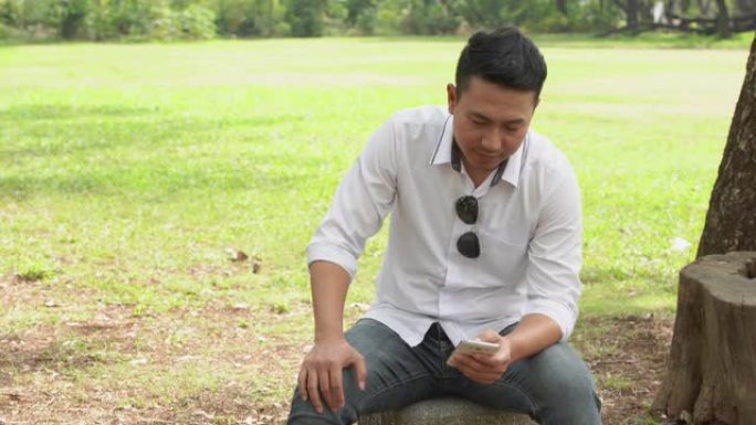 40-50岁的亚洲男性在智能手机上正在公园里阅读一些东西。