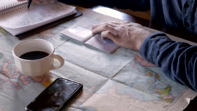 男子在笔记本上写字时看着他的护照邮票和世界地图