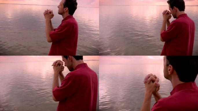 一名男子在日出时在静止的湖泊或海洋中低头祈祷