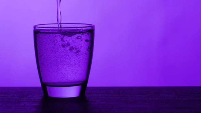 水倒入玻璃并溢出-紫色背景，慢动作