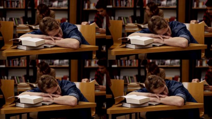 大学图书馆或班级里的年轻欧洲学生睡在桌子上，上面堆着书。背景上的同学和书架