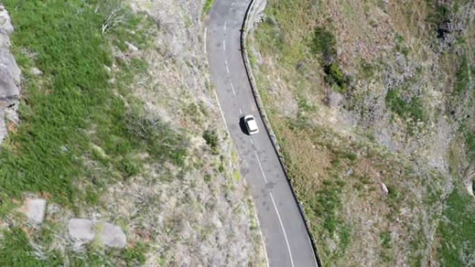 4k顶视图无人机航拍镜头，一辆白色经济型汽车在葡萄牙马德拉岛被悬崖包围的柏油路旁行驶。安全运输概念U